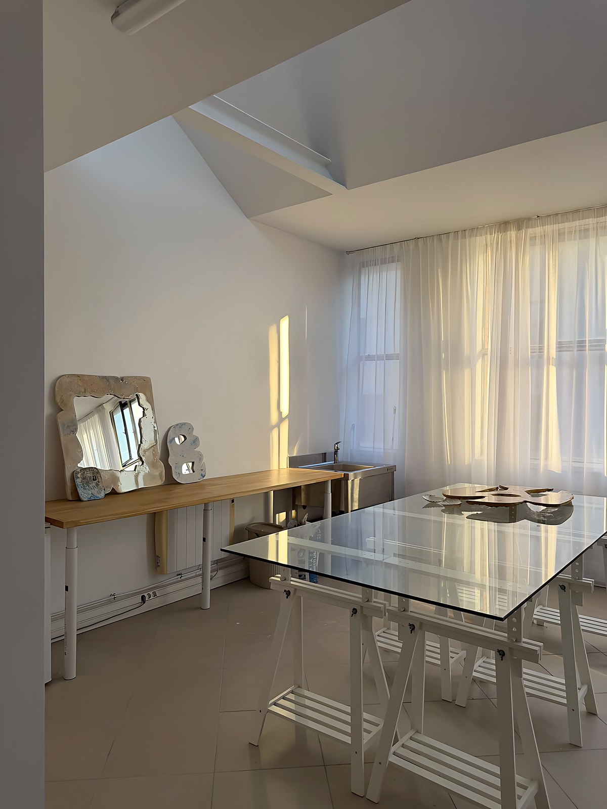 L’atelier : grande table en verre, miroirs posés sur un plan de travail en bois, lumière dorée