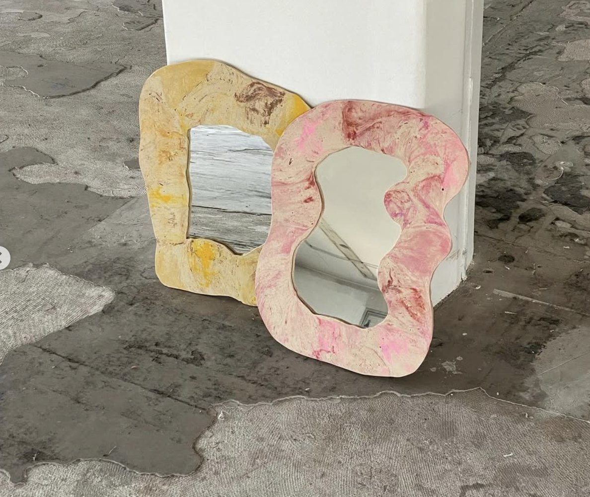 Deux miroirs, jaune et rose, posés au sol contre un pilier