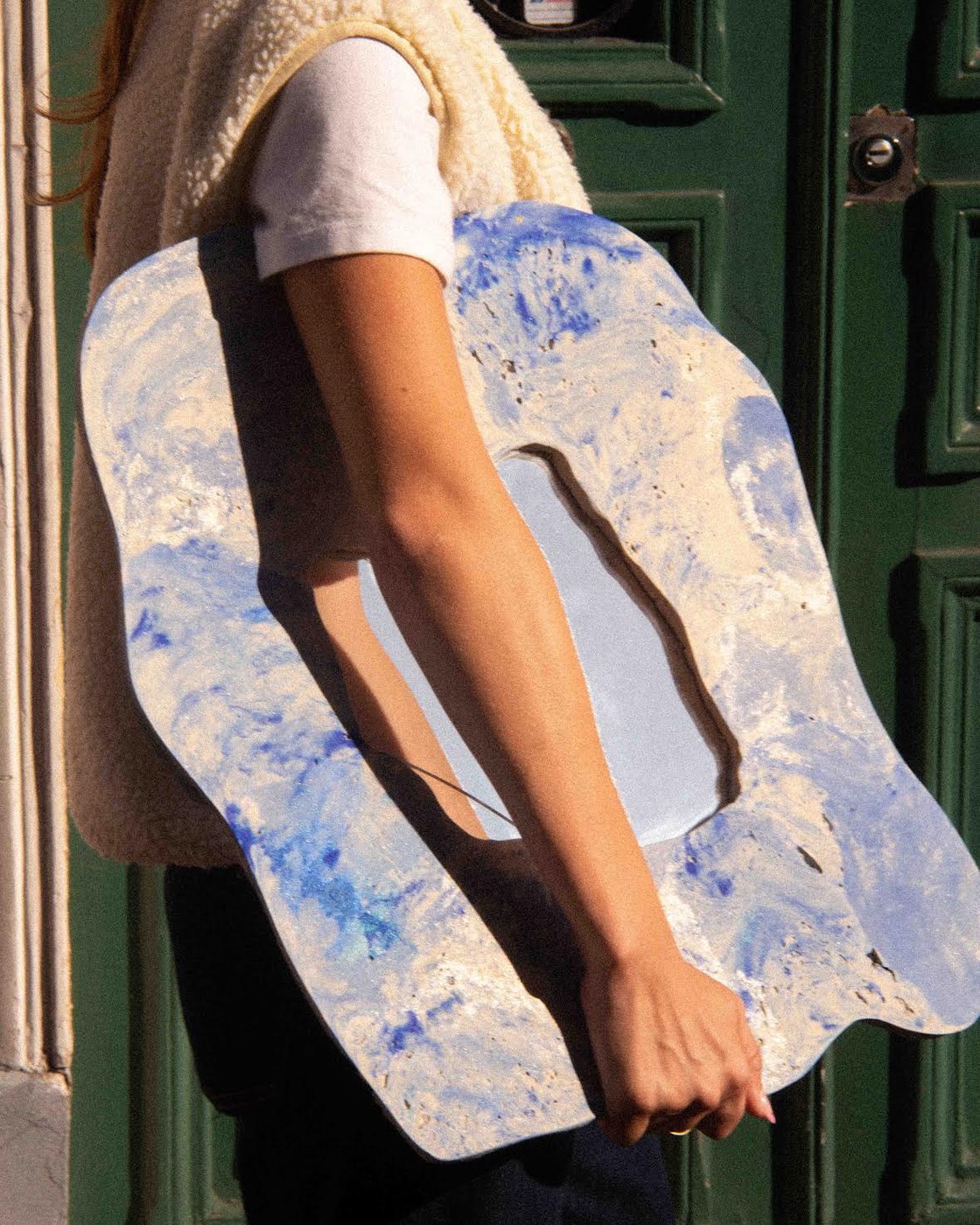 Miroir bleu et blanc porté sous le bras devant une porte verte