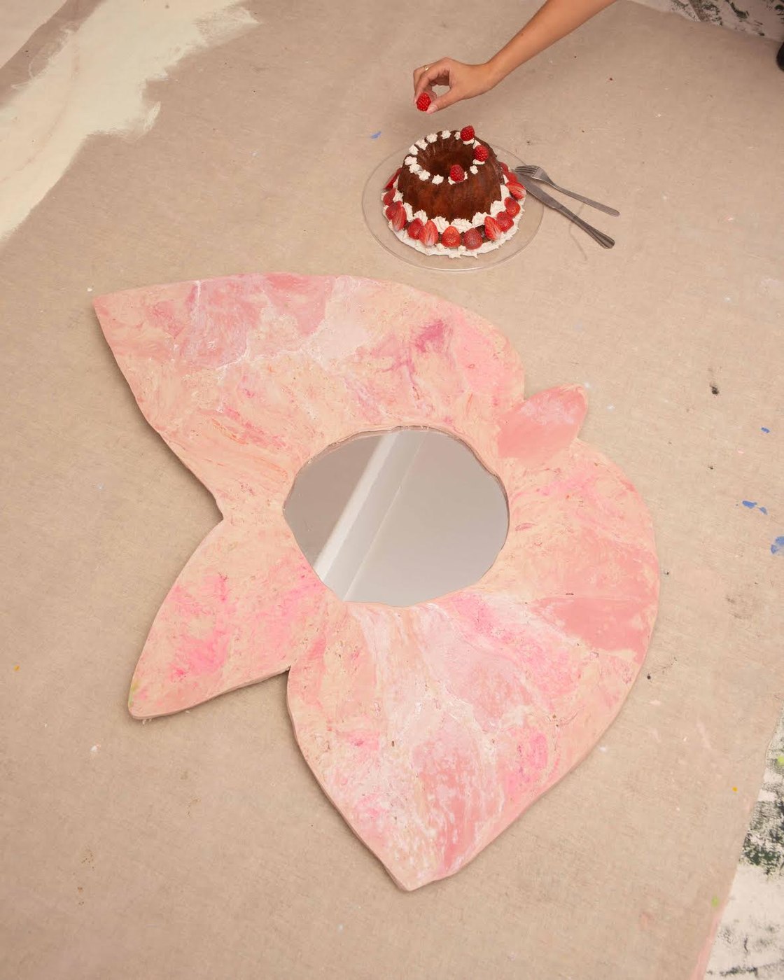 Miroir en forme de fleur rose posé au sol à côté d'un gâteau