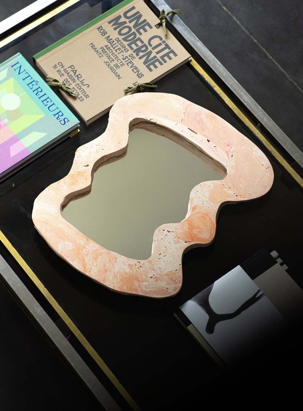 Miroir rose posé sur une table basse noire avec des livres