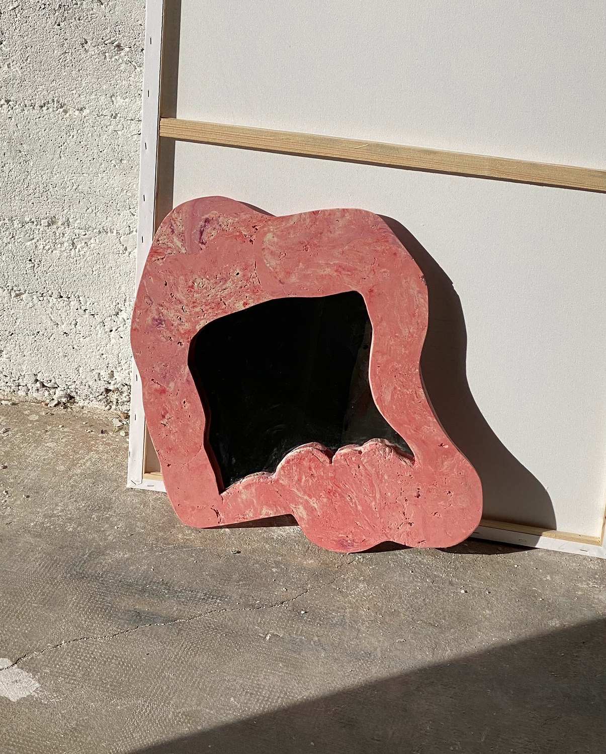 Miroir rose posé contre un mur de béton