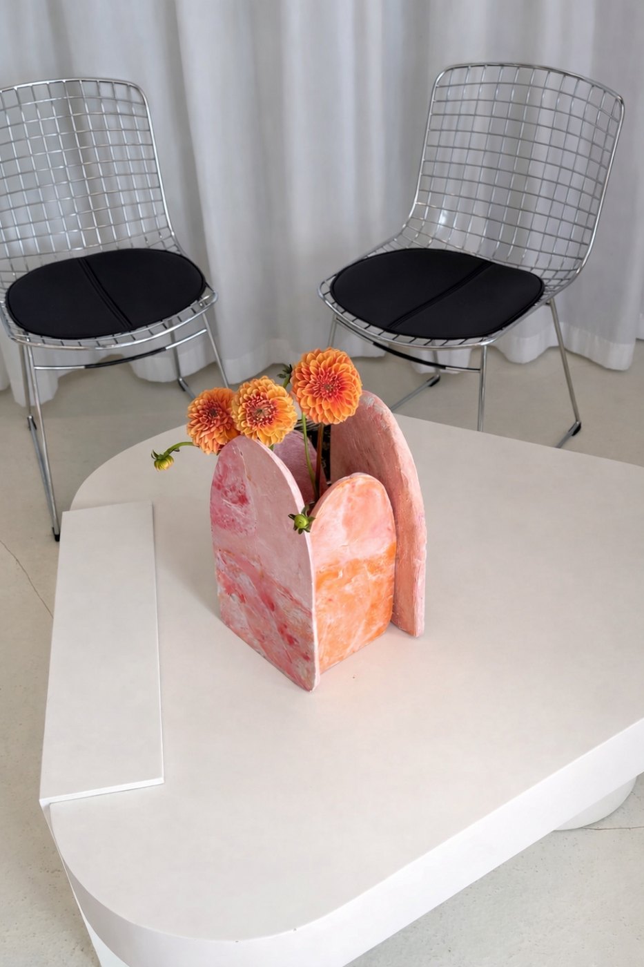Vase en plâtre rose et orange avec des dahlias sur une table blanche